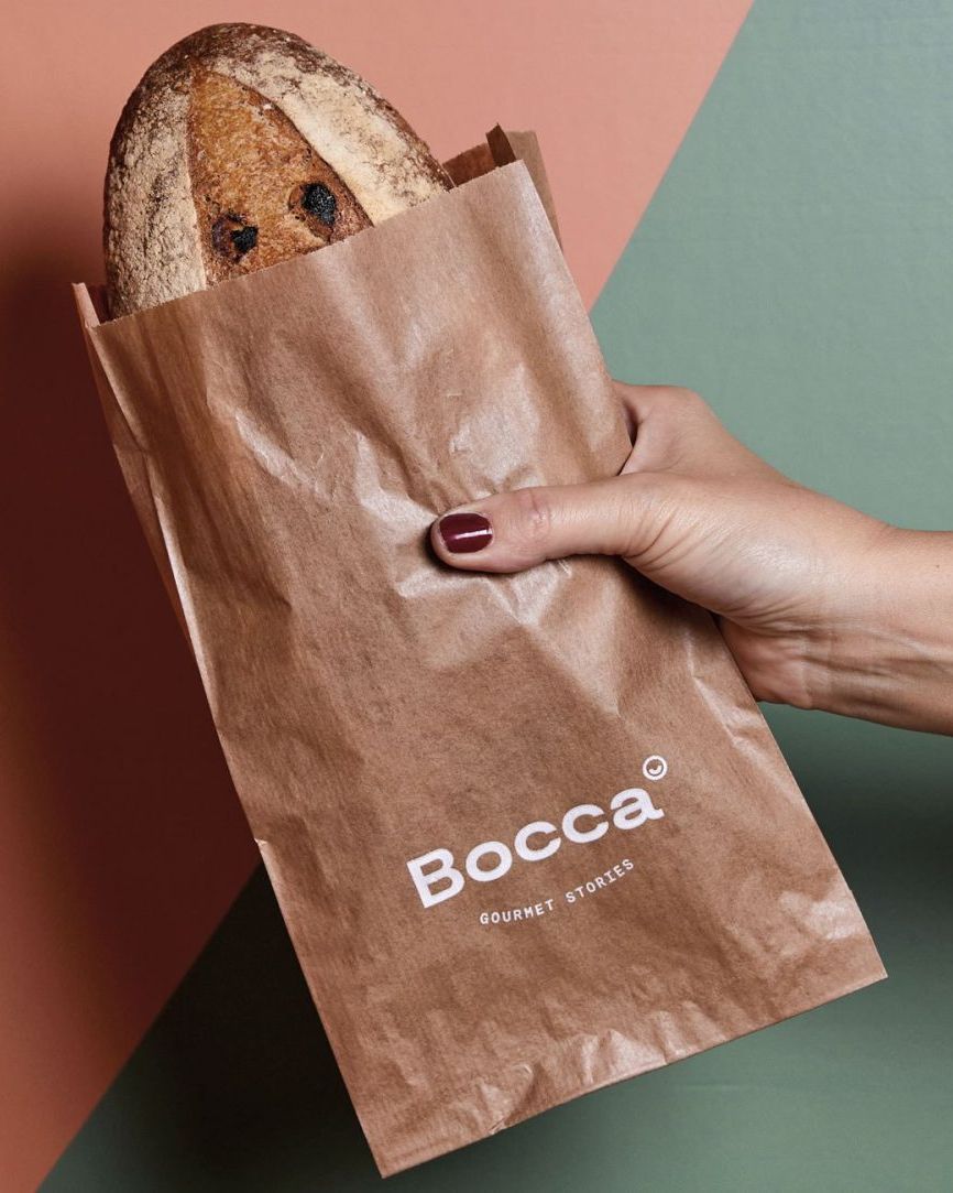 Kenyér egy Bocca Gourmet Stories logós barna papír kenyeres tasakban, kézben tartva